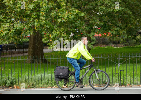 London cycling in Hyde Park UK. Individual cyclist commuter, with clear visible yellow jacket, on the traffic free cycling path Stock Photo
