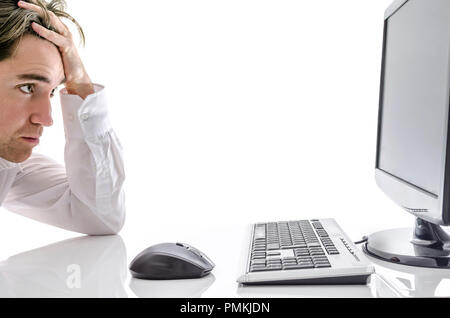 Young businessman sitting at white desk, looking at computer screen. Stock Photo