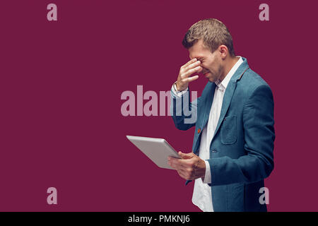 Disappointed man holding tablet and closed eyes with hand. Horizontal studio shot Stock Photo