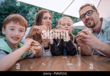 modern family eating hamburgers sitting at a table in a street restaurant