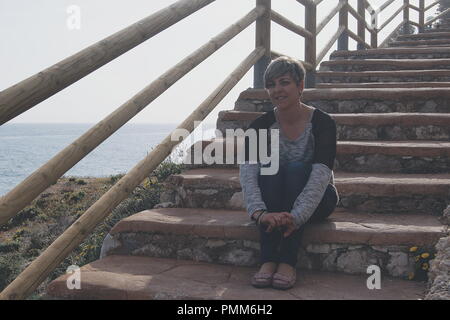Smiling woman sitting on wooden steps by the sea, Malaga, Spain Stock Photo