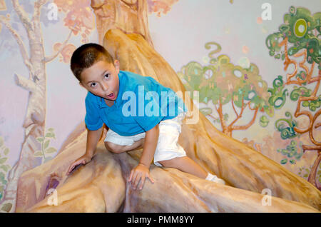 A little surprised boy climbing an indoor tree does not know how to get down Stock Photo