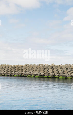 Manmade sea wall / defence / barrier built with blocks of cross-shaped concrete Stock Photo