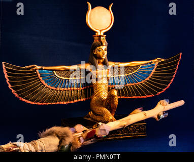 Egyptian goddess Isis kneeling with traditional magic wand made with quartz, amethyst crystals, wood and feathers on dark midnight blue background Stock Photo