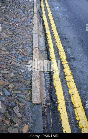 closeup of cobbled pavement, road gutter and  tarmac and yellow painted double line. Stock Photo