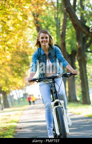 Young woman ride bike in autumn park. Enjoying while cycling in nature during autumn day. Stock Photo