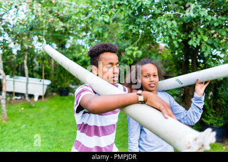 Brother and sister carrying pole in park Stock Photo