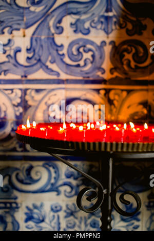 Votive candles burning in a Portuguese church against a backdrop of blue and white ceramic tiles (azulejos) traditional in Portugal Stock Photo