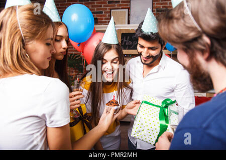 Pretty long hair brunette birthday girl in a party hat celebrating her birthday with the friends Stock Photo