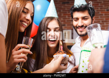 Awesome brunette birthday girl in a party hat laughing and getting ready to blow out the candles on the cupcake Stock Photo