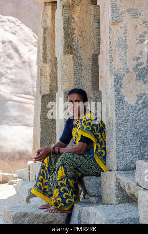 Portrait of a local woman looking at camera while sitting at the entrance of one of the shrines on Hemakuta hill, Hampi, Karnataka, India Stock Photo