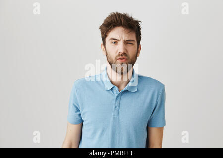 Slow down and tell again. Studio shot of messy sleepy bearded guy feeling puzzled and having no clue what is happening, awakening with hangover and standing over gray background. Stock Photo