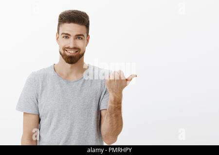 Waist-up shot of handsome stylish and masculine self-assured male with beard and white cute smile pointing right with thumb assuring copy space is perfect with confident delighted expression Stock Photo