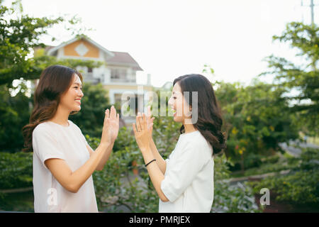 Two beautiful young women giving high five - Pretty girls standing on outdoors and having fun - Best girlfriends making a promise Stock Photo