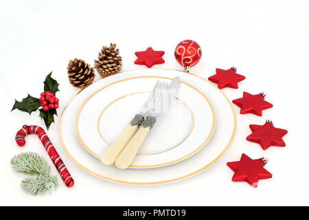 Christmas dinner table setting with white porcelain plates, cutlery, bauble decorations and winter holly and fir on white background. Stock Photo