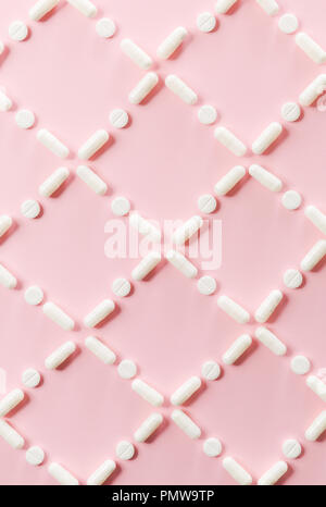 Pattern of white pills and tablets on a pink background. Stock Photo