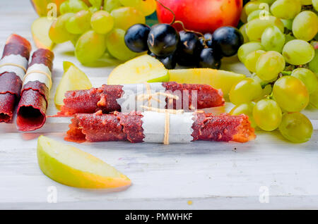 Fresh yellow apples, white and blue grapes, scattered on the  table, slice fruits and fruit leather rolls on white wooden table. Detox concept. Health Stock Photo