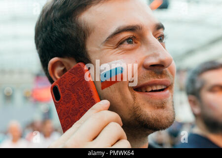 Russian fan with a painted national flag on his cheek, on FIFA Football World Cup in Moscow supporting national team, while talking on mobile phone Stock Photo