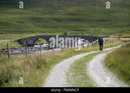 Man Walking and Garva Bridge on the Corrieyairack Pass part of General Wades Military Road on Route to the Scottish Mountain Corbett Meal na h-Arsre. Stock Photo