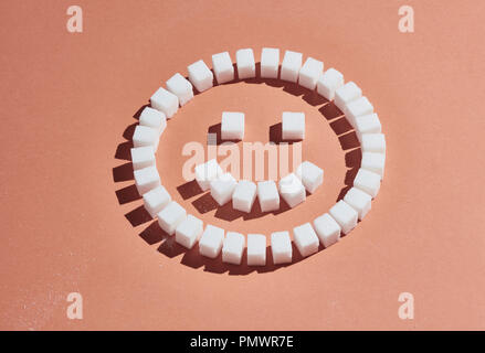 Sugar cubes forming smiley face on peach background Stock Photo