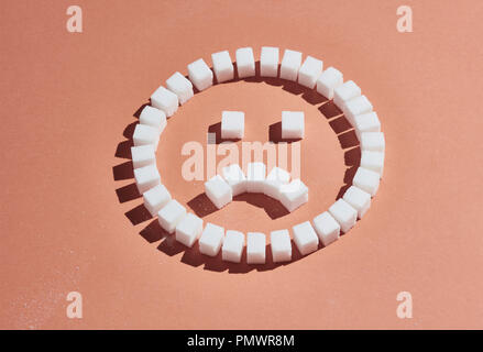 Sugar cubes forming frowning face on peach background Stock Photo