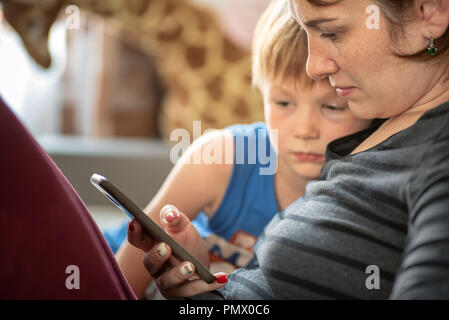Mother and son using smartphone tablet on sofe at home. Stock Photo