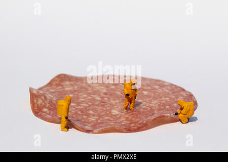 Small scientists in clean suits examining salami for bacteria Stock Photo