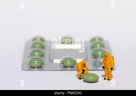 Small scientists in clean suits examining green pill from blister pack Stock Photo