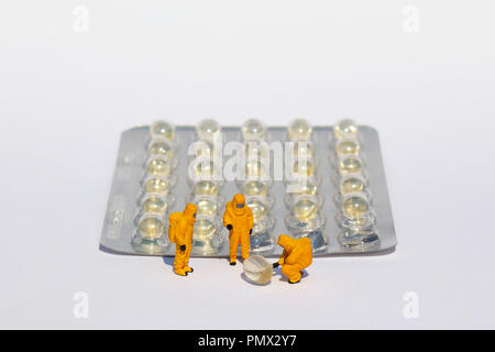 Small scientists in clean suits examining gel capsules from blister pack Stock Photo