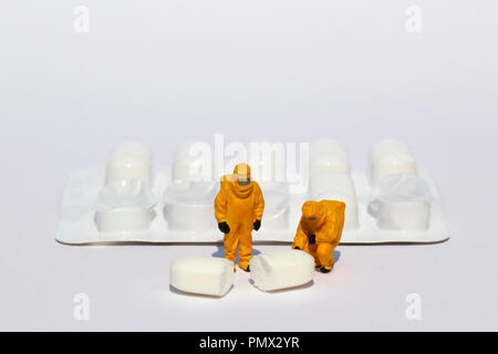 Small scientists in clean suits examining white tablet from blister pack Stock Photo