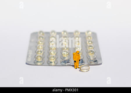 Small scientists in clean suits examining gel capsules from blister pack Stock Photo