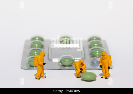 Small scientists in clean suits examining green pill from blister pack Stock Photo