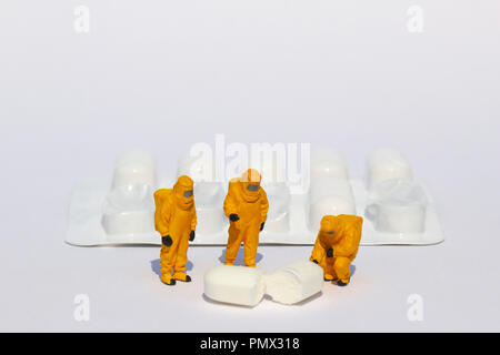 Small scientists in clean suits examining white tablet from blister pack Stock Photo