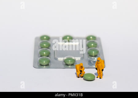 Small scientists in clean suits examining green pill from blister pack Stock Photo