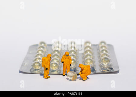Small scientists in clean suits examining gel capsules from blister pack Stock Photo