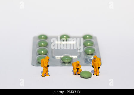 Small scientists in clean suits examining green pill from blister pack Stock Photo