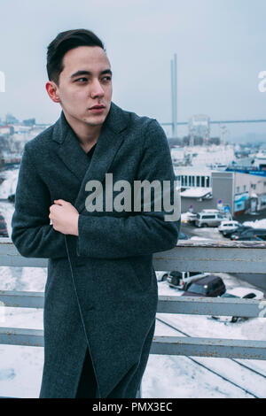 Young man in long coat on urban winter bridge Stock Photo