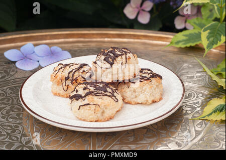 Chocolate drizzled home made recipe gluten free coconut macaroons on Poole plate and Turkish brass tray outside ready to be eaten, in garden Stock Photo