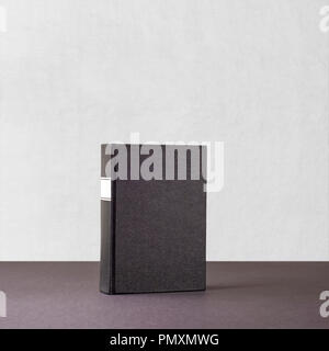 Black book with whiteframe on spine standing a dark paper surface near the white wall Stock Photo