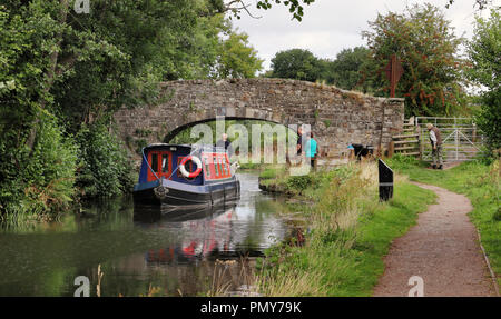 Stone Bridge over the Brecon and Monmouthshire canal in South Wales with narrowboat and walkers on the Tow Path Stock Photo