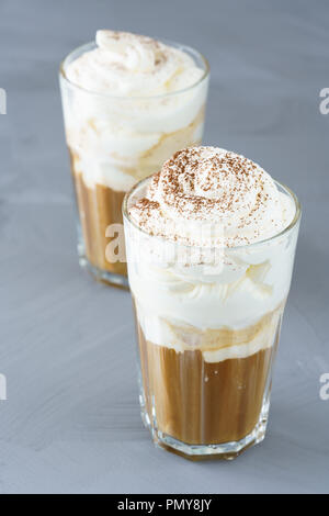 Ice coffee topped with vanilla ice cream, whipped cream and grated chocolate. Gray table, high resolution. Stock Photo