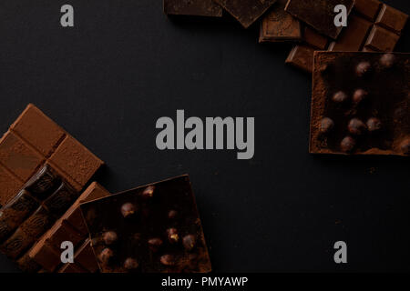 top view of assorted delicious chocolate pieces with hazelnuts on black background Stock Photo