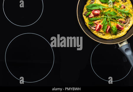 top view of omelette in frying pan cooking on black stove Stock Photo