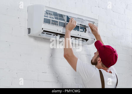 young repairman changing filter for air conditioner hanging on white brick wall Stock Photo