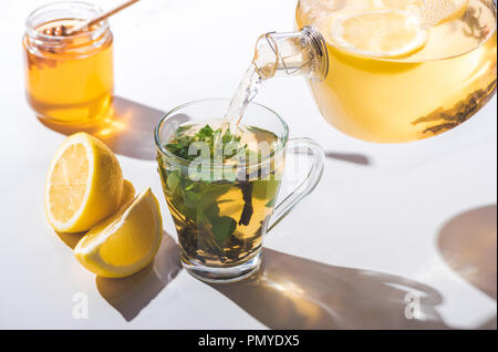pouring healthy tea with lemon and mint from teapot into cup on white tabletop Stock Photo