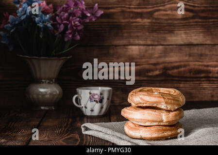 Eclairs stack on table with cup of coffee and vase of flowers Stock Photo
