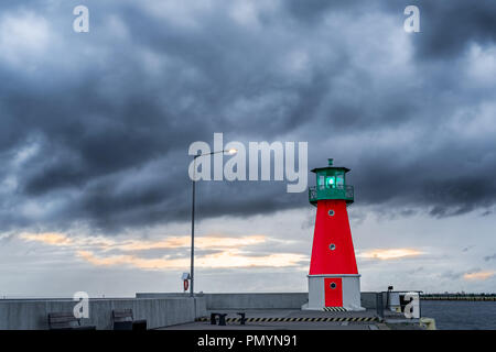 Red and green lighthouse on a harbor pier against dramatic clouds in the sky. Stock Photo