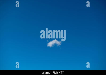 Single small 'C' shaped cloud and resembling an eyebrow, in a deep blue sky. Stock Photo