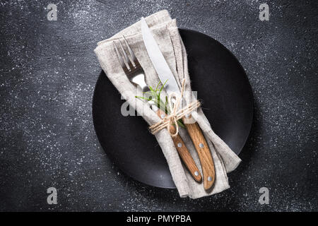 Black plate, cutlery and napkin on stone table top view. Stock Photo