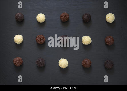 Fancy dark milk white chocolate truffles ready to eat on black stone background. Stock Photo